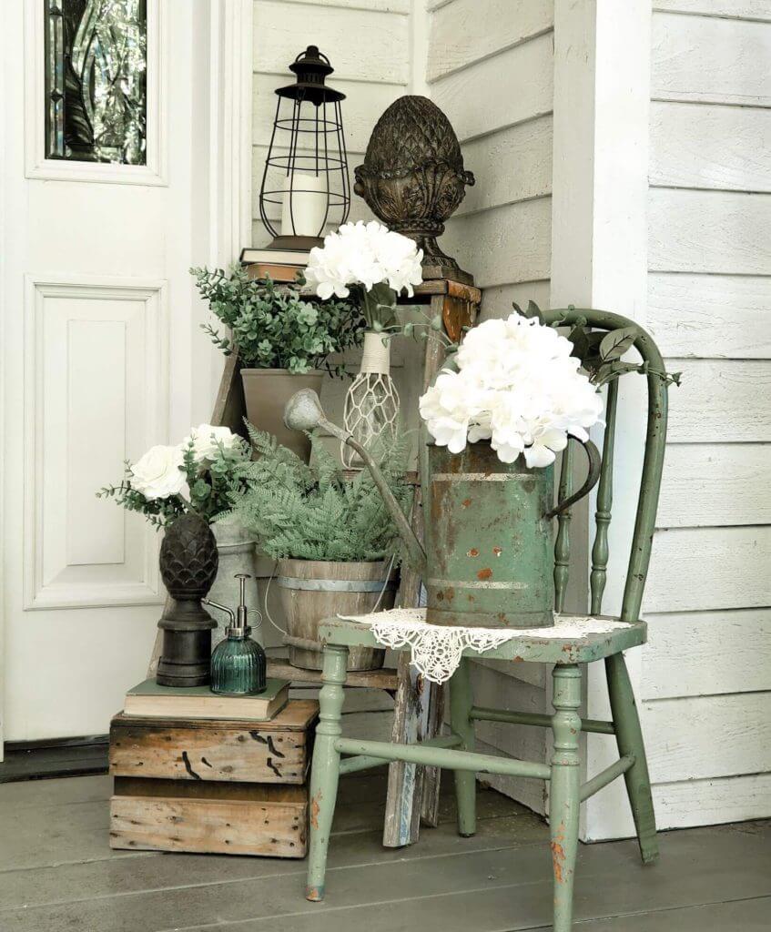 Decoración de porche rústica con silla verde, macetas y flores blancas.