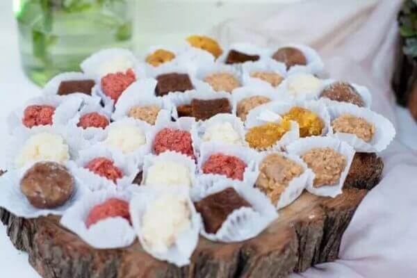 Plato de madera rústica con trufas de chocolate y bombones de coco para mesa dulce.