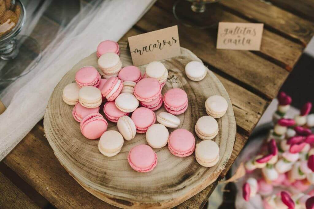 Deliciosos macarons rosados y blancos presentados sobre un plato de madera, postres para bodas.