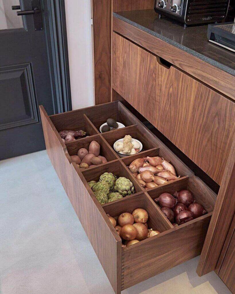 Organizador de cajón de madera con compartimentos para patatas y cebollas en la cocina.