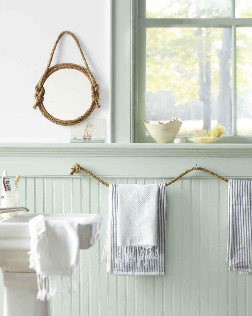 Baño con temática náutica: Espejo redondo con marco de cuerda, toallas a rayas y decoración marinera.