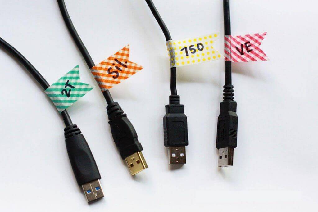 Cables USB etiquetados: Cuatro conectores organizados con banderines de colores y letras manuscritas.