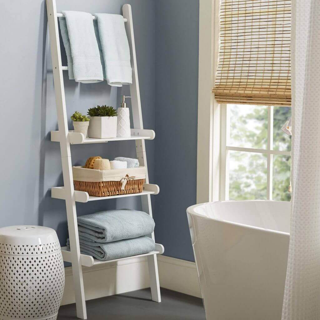 Estante blanco en baño: Toallas, plantas y accesorios de higiene organizados junto a cesta y bañera.