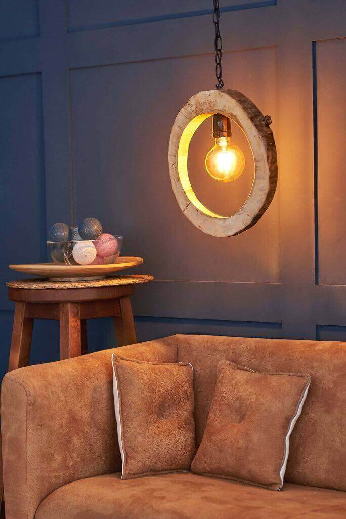 Lámpara colgante circular con luz cálida sobre mesa rústica y sofá de ante marrón.