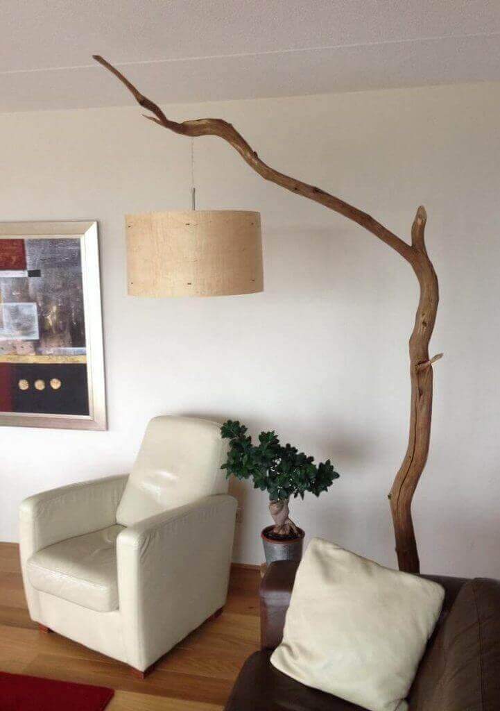 Lámparas con troncos en salón moderno con sofá de cuero, arte abstracto y planta verde.