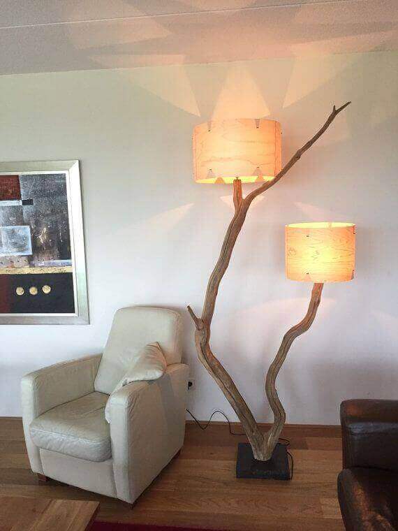 Lámparas con troncos y luz cálida junto a sillón blanco en salón moderno con arte abstracto.
