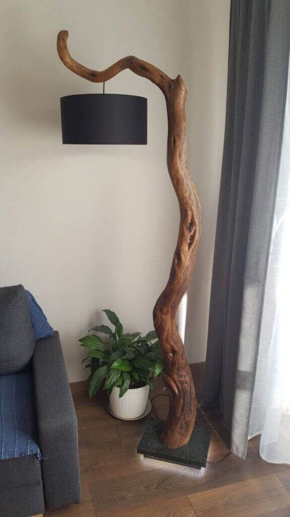 Lámparas con troncos de diseño rústico junto a sofá gris y planta en salón elegante.