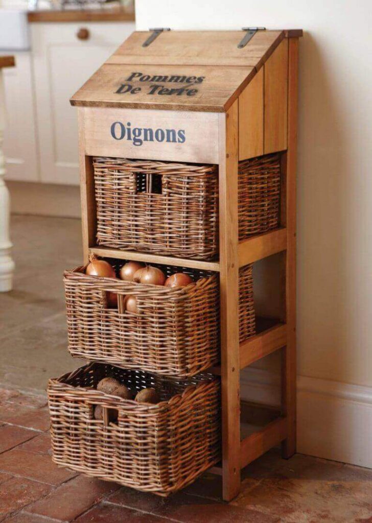Mueble auxiliar rústico con cestas de mimbre para almacenar patatas y cebollas en la cocina.